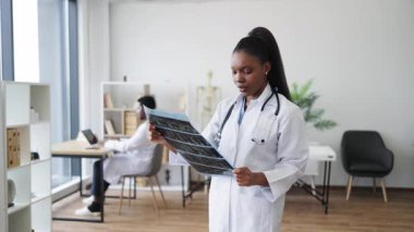 Beyaz laboratuvar önlüğü giyen profesyonel bir kadın doktor başka bir doktor geçmişine sahip röntgen görüntüsünü analiz ediyor. Modern bir klinikte kapalı bir yere yerleşmek. Olay yeri sağlık, araştırma ve kesinlik sunar.