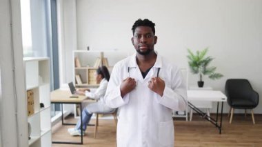 Steteskoplu beyaz önlük giyen erkek doktor ofiste olumlu bir jest yapıyor. Modern klinikte çalışan başka bir tıp uzmanı. Sağlık ve profesyonelliği temsil ediyor