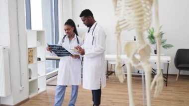 Odaklanmış erkek ve kadın doktorlar röntgen görüntülerini analiz ediyor, ön planda tıbbi iskelet, çevreyi inceliyor..