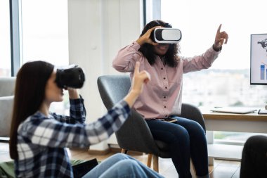 Women interacting with virtual reality technology wearing VR glasses in office setting. Exploring immersive digital experience, modern technology engaging workplace activities.