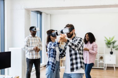 Young adults wearing VR headsets engaged in interactive activity, simulating dance and entertainment. Group consisting of men and women having fun with innovative wearable technology.