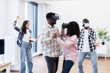 Young adults wearing virtual reality headsets interacting playfully in a modern room creating joyful and innovative moments. Engaged in technology and entertainment, embracing contemporary leisure.