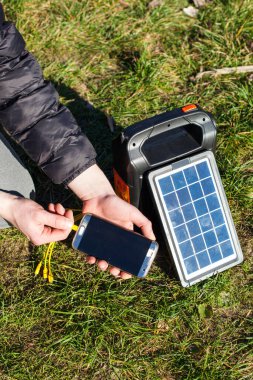 Bir adam telefonunu doğada şarj ediyor. El feneri ve telsizi olan küçük bir elektrik santrali güneşin enerjisiyle şarj edilir. Taşınabilir güç tedarik sistemiyle dağlarda geziniyor. Dikey fotoğraf