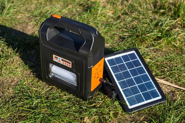 A portable power bank with a flashlight, radio and USB ports for charging the phone. The power bank is charged by a solar panel. Portable power plant in nature in sunny weather.