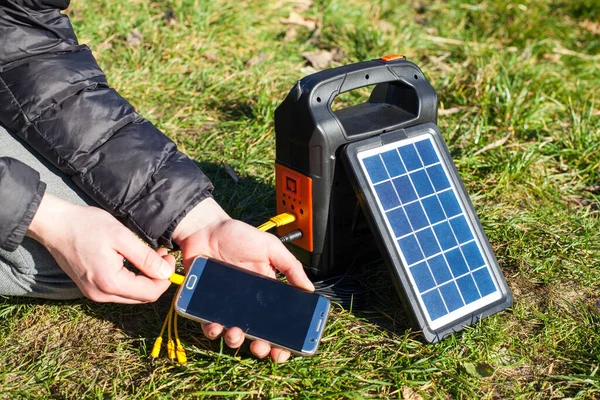 在阳光明媚的日子里 太阳能电池板给手机充电 电话在一个充电的人手里 徒步旅行和旅游的便携式动力库 图库图片