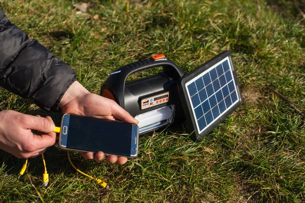 这名男子左手拿起电话 放在一个由太阳能电池板供电的便携式电站的充电器上 有手电筒和太阳能板驱动的板的电站 图库图片