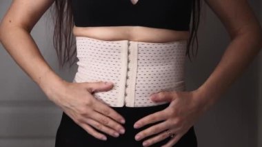 Diastasis hastası bir kadın. Nefes egzersizleri sırasında karnı düz olan kız vücut esnekliği yapıyor. Göbeğe yakın çekim. Bel omurgasında destekleyici korse. Yüz tanınmaz halde.