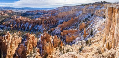 Panorama of Bryce Canyon accented in freshly fallen snow and distant mountains and brilliantly colored orange cliffs.
