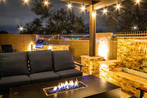 A resort style backyard at night with a waterfall, pergola, and a firepit at night.