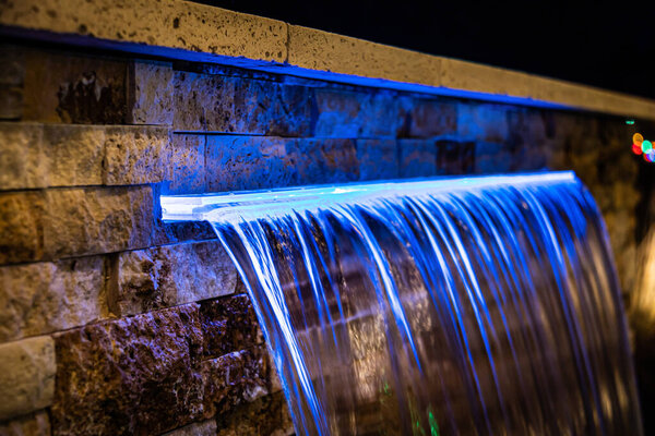A close-up of an illuminated home waterfall at night against a stacked stone background.