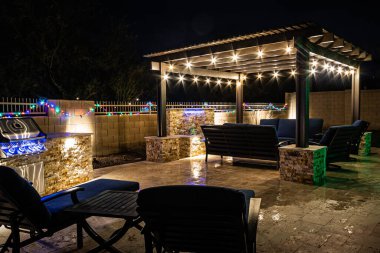 A resort style backyard at night with a waterfall, pergola, and a firepit at night.