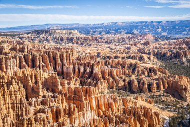 Bryce Canyon accented in freshly fallen snow and distant mountains and brilliantly colored orange cliffs.