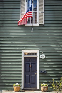 Sömürge tarzı bir evin kapısında gün ışığında yeşile boyanmış bir Amerikan bayrağı asılı..