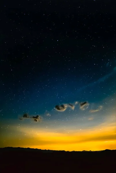 遠くの都市の光害を通して輝く夜空の星々とシルエットの山 — ストック写真