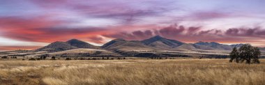 Uzak bir dağ silsilesinin manzarası. Tepeler çimlerle kaplıydı. Arizona 'da dramatik bir gün batımı vardı..