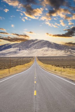 Gün batımına doğru giden uzun, düz bir yol ve Idaho 'daki uzak dağlar..