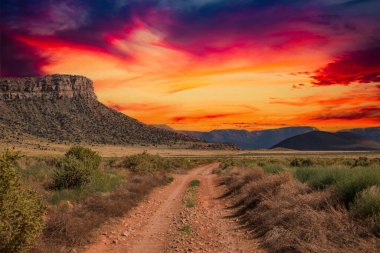 Uzak dağlara giden kırsal bir toprak yol dramatik bir günbatımı ile.