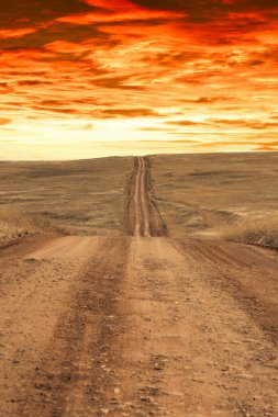 Gün batımında ufukta görünen uzak bir tepenin üzerinden geçen toprak bir yol..