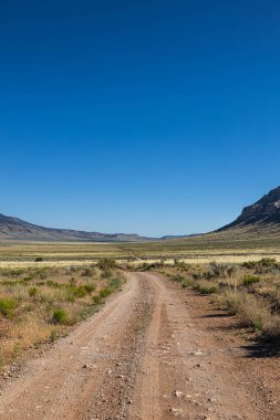Kuzey Arizona 'da engin kurak bir vadi boyunca uzanan toprak bir yol berrak mavi bir gökyüzü ile.
