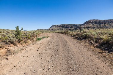 Kuzey Arizona 'da engin kurak bir vadi boyunca uzanan toprak bir yol berrak mavi bir gökyüzü ile.