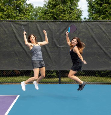 Two pickleball players jumping with paddles on a court during summer. clipart