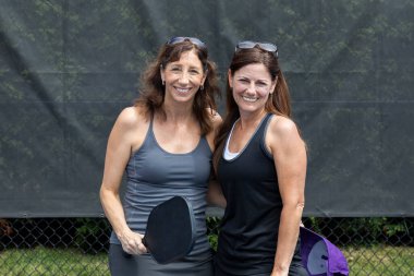 Two pickleball players posing with paddles on a court during summer.
