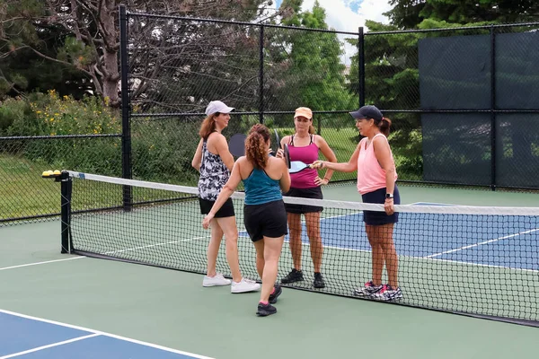 Four female pickleball players touch paddles after a competitive game.