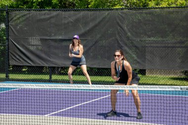 A pickleball player prepares for a return of serve on a suburban pickleball court during summer.