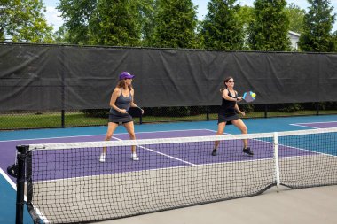 Two pickleball players in action on a suburban pickleball court during summer.