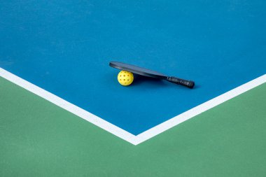 View of a pickleball paddle and yellow ball on a blue and green court with white lines. clipart
