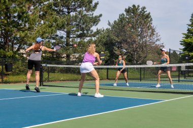 Bir comptetivie, yazın mavi ve yeşil bir kortta, kalede iki misli pickleball oynuyor..