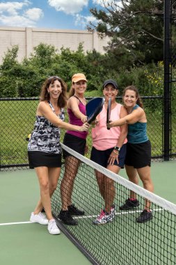 Four female pickleball players touch paddles after a competitive game.