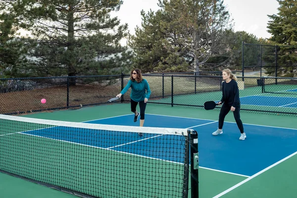 A female pickleball player returns a volley on a blue and green court as her partner looks on..