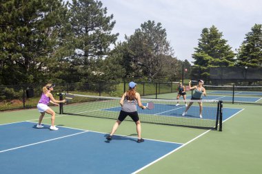 Pickleball oyuncusu, mavi ve yeşil bir kortta rakiplerini ezmeye hazırlanıyor..