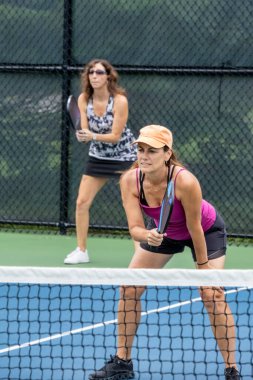 Two pickleball players prepare to return a ball on a suburban pickleball court during summer.