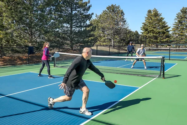 プレイヤーは春に青と緑の裁判所に男性と女性のグループとピックボールの試合を2倍に競争の中でバックハンドを打つ — ストック写真