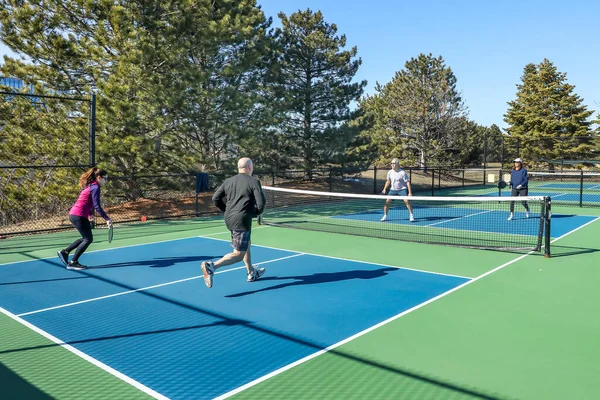 プレイヤーは春に青と緑の裁判所に男性と女性のグループとピックルボールの試合を2倍に競争でフォアハンドを打つ ロイヤリティフリーのストック写真