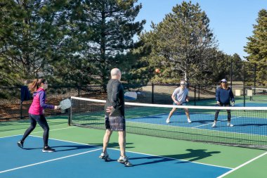 A comptetivie doubles game of pickleball at the net with a group of men and women on a blue and green court in spring. clipart