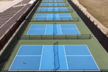 Baharın başında bir banliyö parkında mavi ve yeşil kortlu yeni bir Pickleball tesisinin havadan görünüşü.