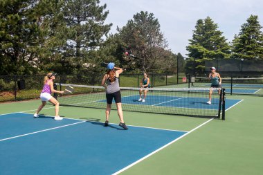 Bir comptetivie, yazın mavi ve yeşil bir kortta, kalede iki misli pickleball oynuyor..