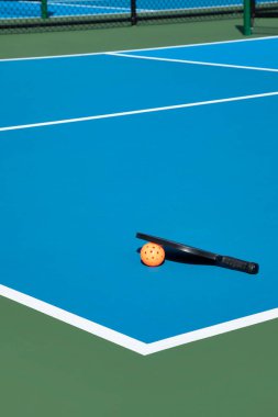 View of a new pickleball complex with a paddle and orange ball on blue and green courts in a suburban setting during early spring. clipart