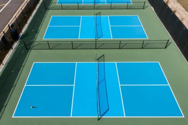 Baharın başında bir banliyö parkında mavi ve yeşil kortlu yeni bir Pickleball tesisinin havadan görünüşü.