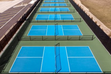 Baharın başında bir banliyö parkında mavi ve yeşil kortlu yeni bir Pickleball tesisinin havadan görünüşü.