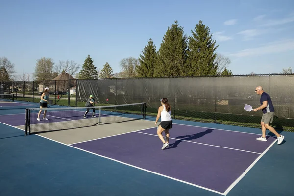 A female pickleball player hits a volley at the net as her opponents prepare to return the ball on a dedicated court at a public park.