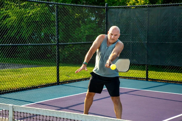 A male pickleball player returns a volley at the net on a dedicated court at a public park.