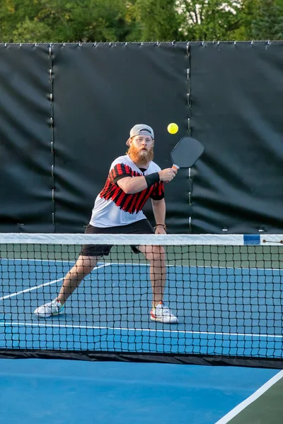 A male pickleball player returns a volley at the net with his backhand on a dedicated court at a public park.