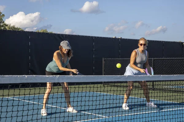 一个女泡菜手在她的搭档看着球的时候在网球场上打了一个截击 — 图库照片