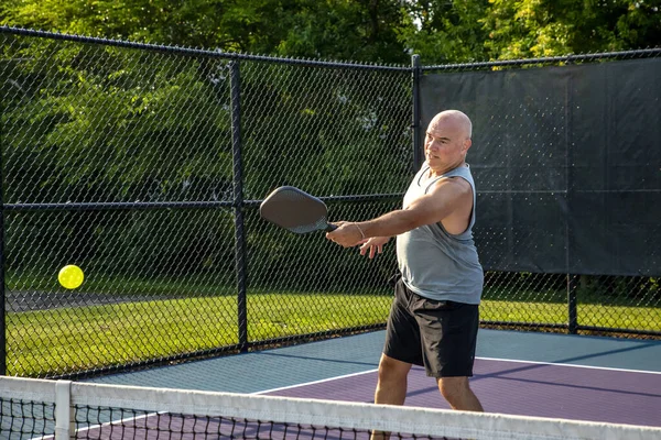 A male pickleball player drives a volley at the net on a dedicated court at a public park.