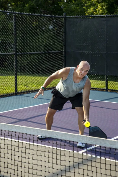 A male pickleball player returns a volley at the net on a dedicated court at a public park.