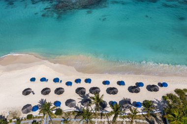 Anguilla 'da Shoal Bay Sahili boyunca şemsiyeli ve palmiye ağaçlı turkuaz suların havadan görüntüsü..